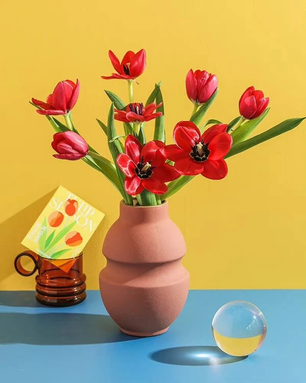 một chiếc bình với hoa màu đỏ và một tấm thiệp ảnh hoa tulip